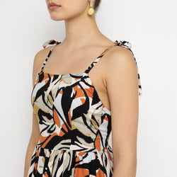 Close-up side view of a woman wearing a tropical leaf print mini dress with tie-up spaghetti straps in black, orange, and beige tones.