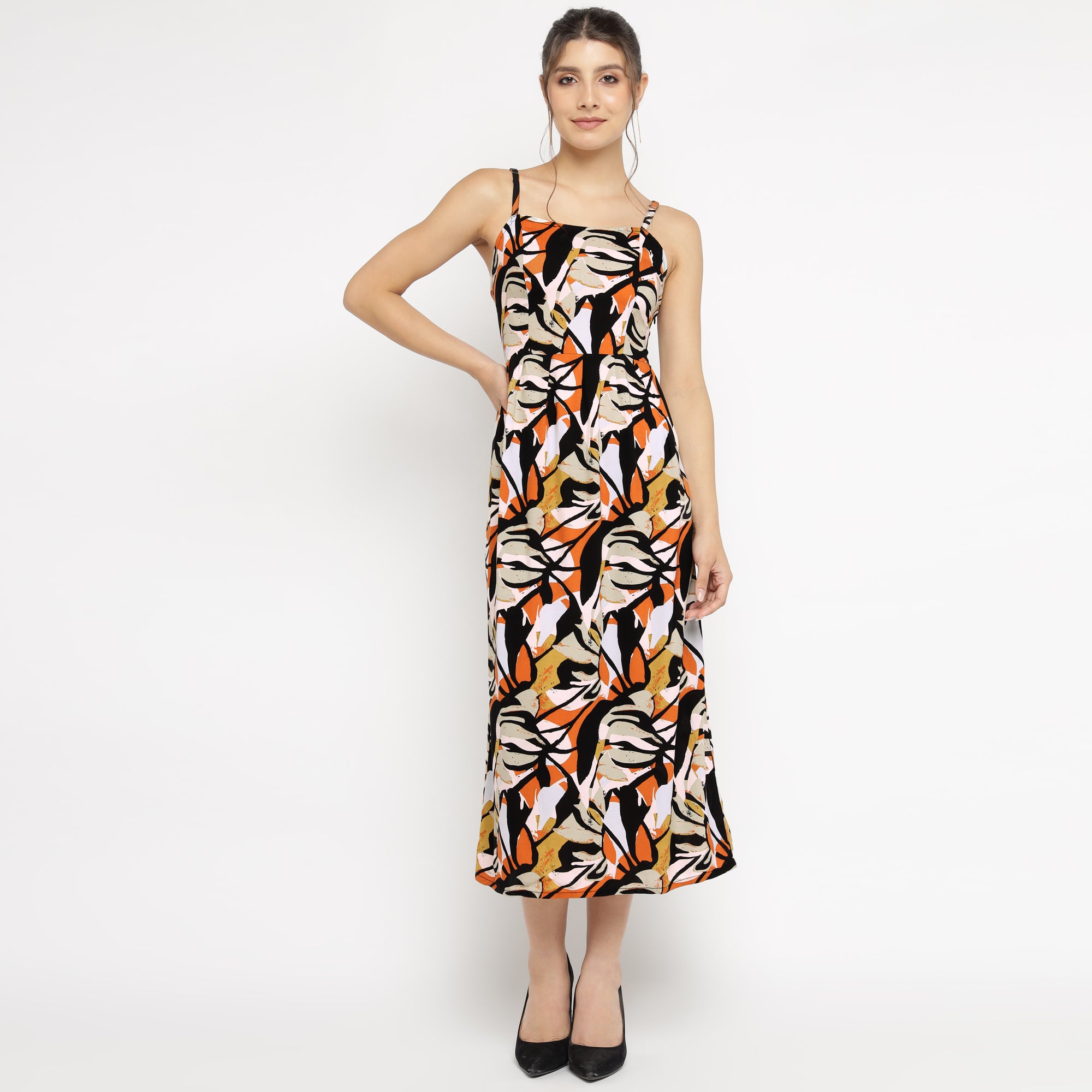 Front view of a woman posing in an abstract floral print midi dress with spaghetti straps, styled with black heels, against a plain white background.