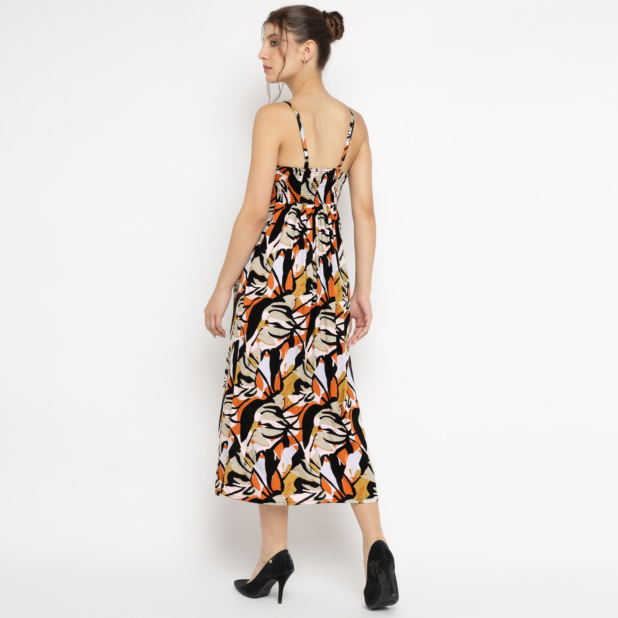 Back view of a woman wearing an abstract floral print midi dress with spaghetti straps and black heels, standing against a white background.