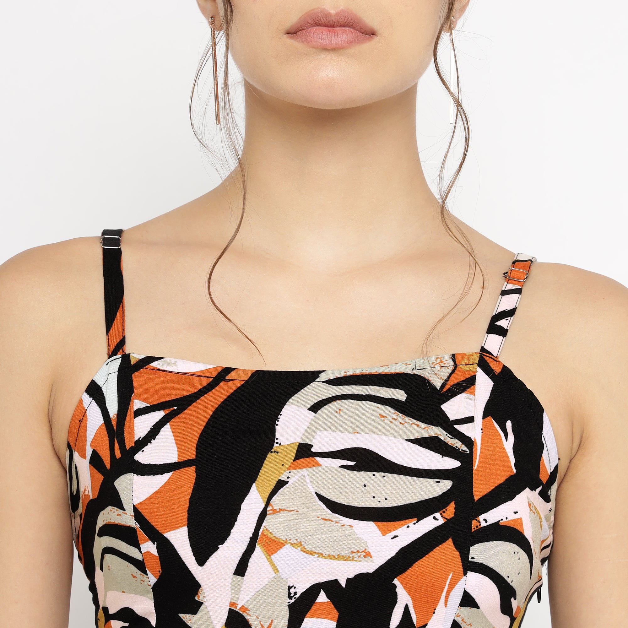 Close-up of a woman wearing a sleeveless abstract floral print dress with spaghetti straps in black, orange, white, and beige.