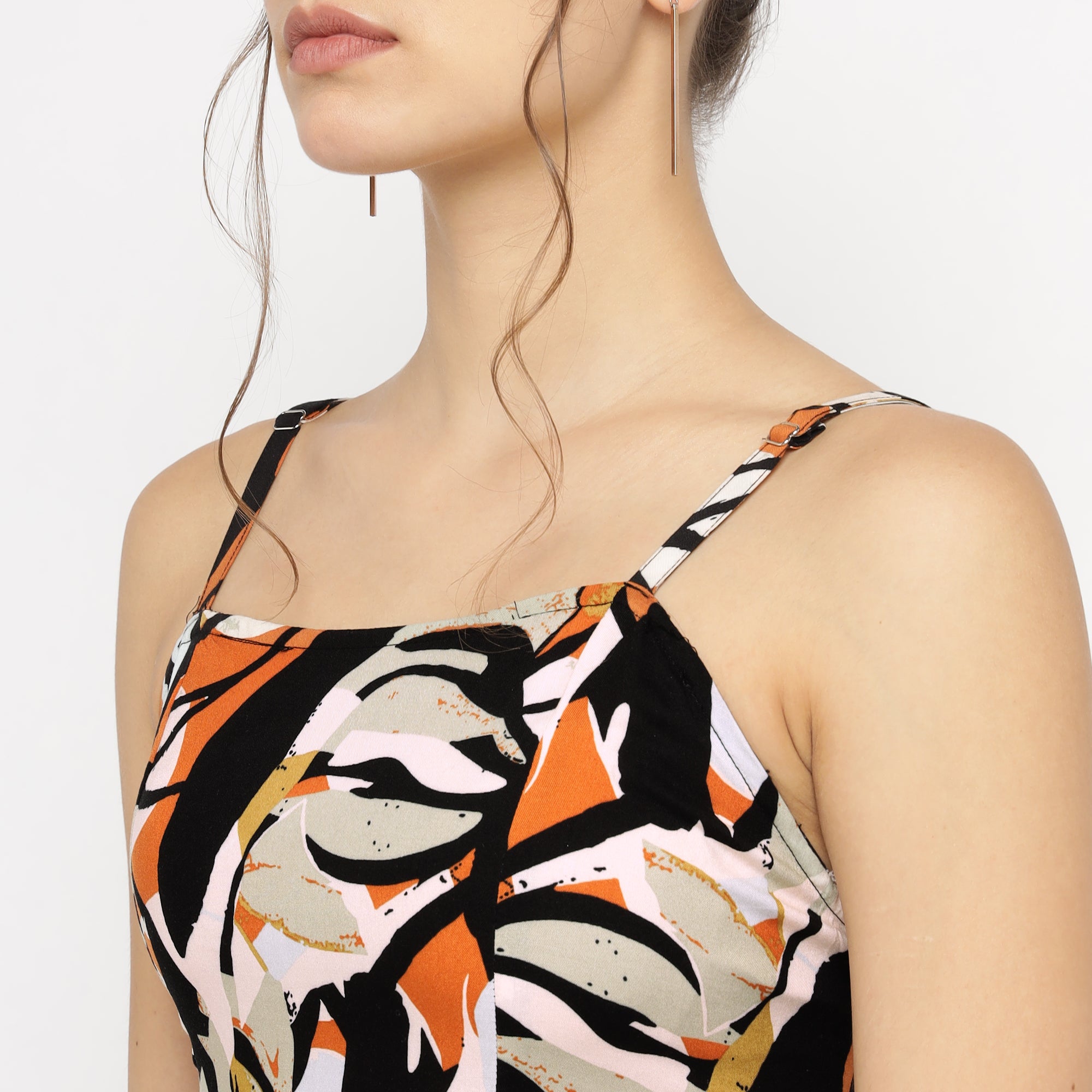 Model wearing an abstract floral print midi dress with spaghetti straps in shades of orange, black, and beige.