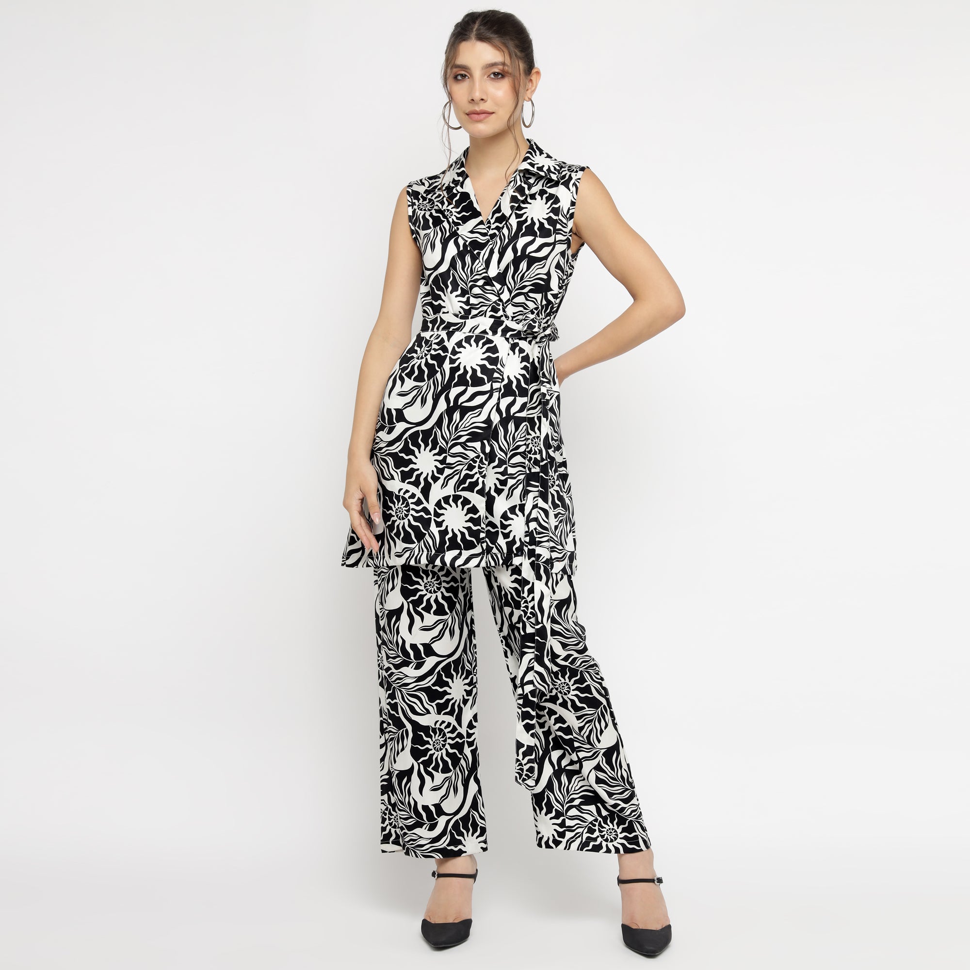 Model wearing a black and white abstract printed sleeveless co-ord set, featuring a collared V-neck top paired with wide-leg trousers. The outfit showcases a bold, artistic floral design and is styled with black heels against a plain white background.