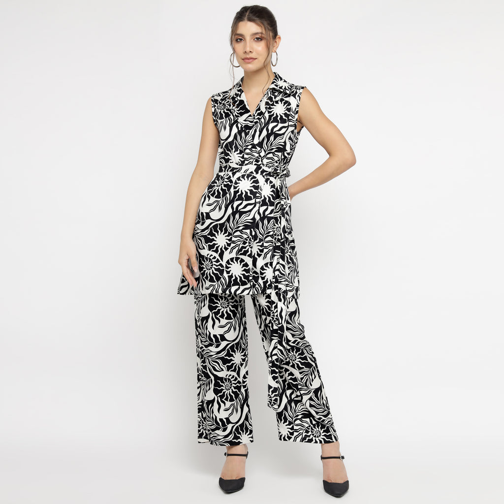 Model wearing a black and white abstract printed sleeveless co-ord set, featuring a collared V-neck top paired with wide-leg trousers. The outfit showcases a bold, artistic floral design and is styled with black heels against a plain white background.