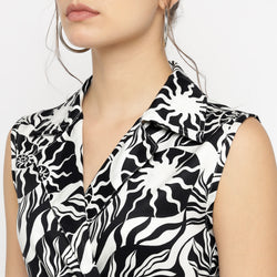 Close-up of the upper portion of a sleeveless collared top from a black and white abstract printed co-ord set, highlighting the textured fabric and intricate pattern details around the neckline and shoulders. The model's face is partially visible, styled with a loose bun and hoop earrings.









