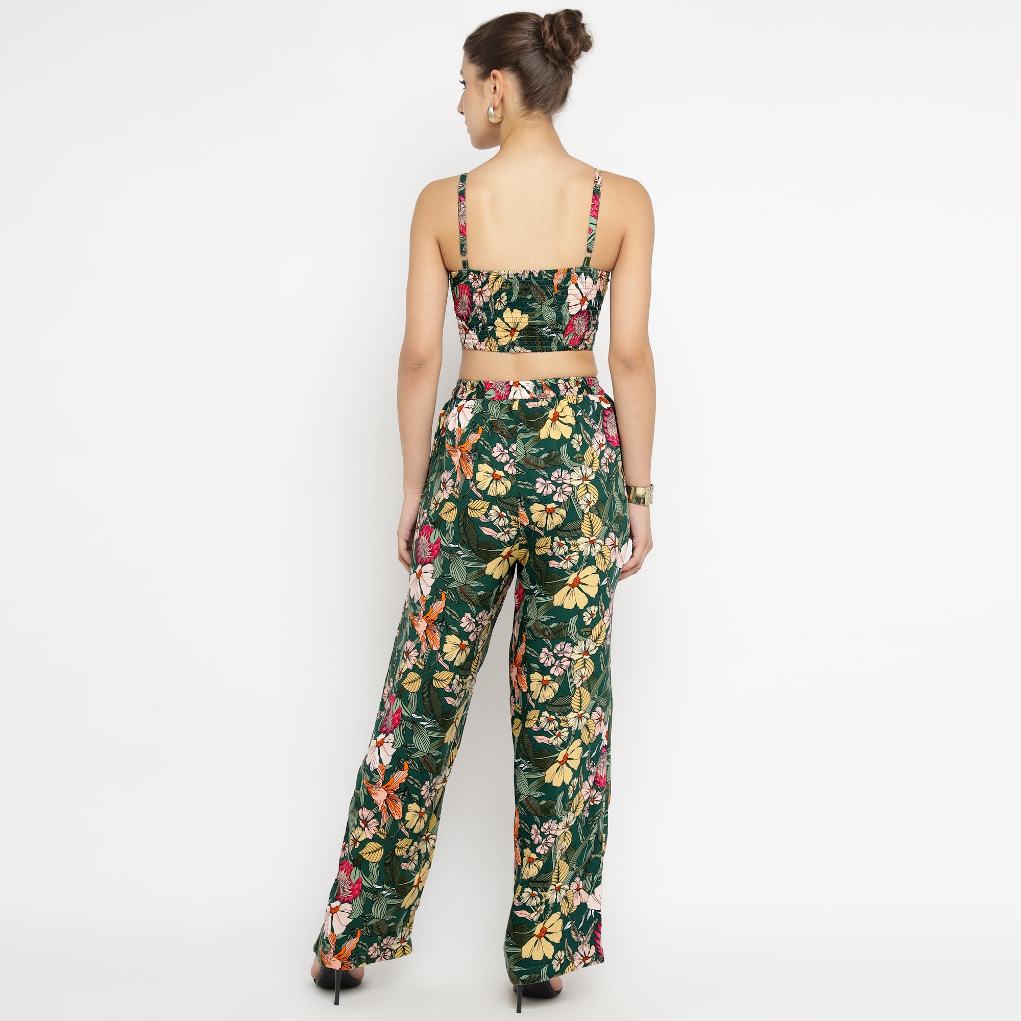 Back view of a model wearing the Tropical Bloom Co-ord Set, consisting of a sleeveless crop top with thin shoulder straps and high-waisted wide-leg pants. The co-ord set features a lush tropical floral pattern in green, yellow, pink, and red tones. The model is standing against a white background with hands resting at her sides, showcasing the rear design and fit of the outfit.