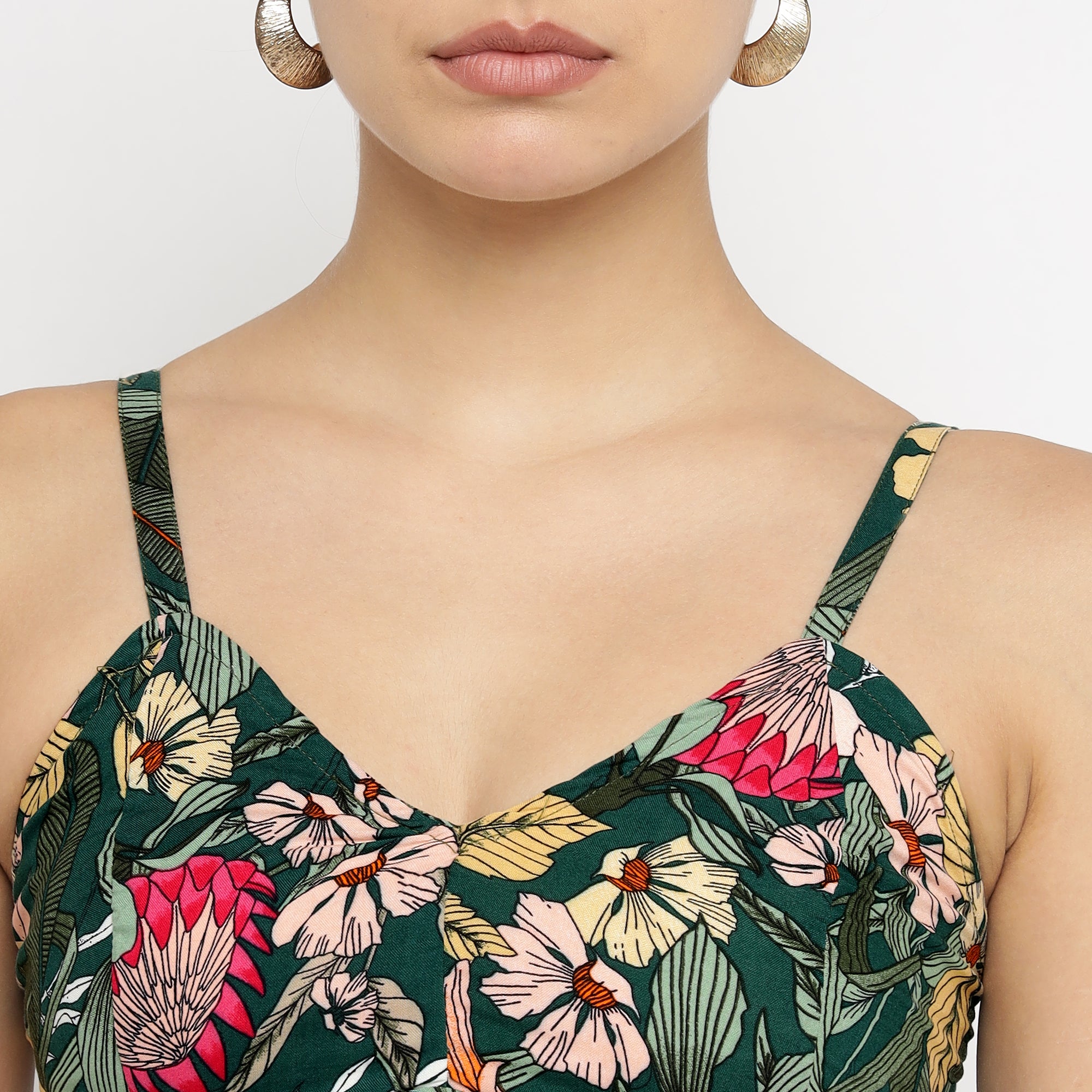 Close-up view of the upper bodice of the Tropical Bloom Co-ord Set, showcasing a sleeveless, V-neck top with thin shoulder straps. The fabric features a vibrant tropical floral print in shades of pink, yellow, red, and white on a deep green background. The model is accessorized with large hoop earrings.