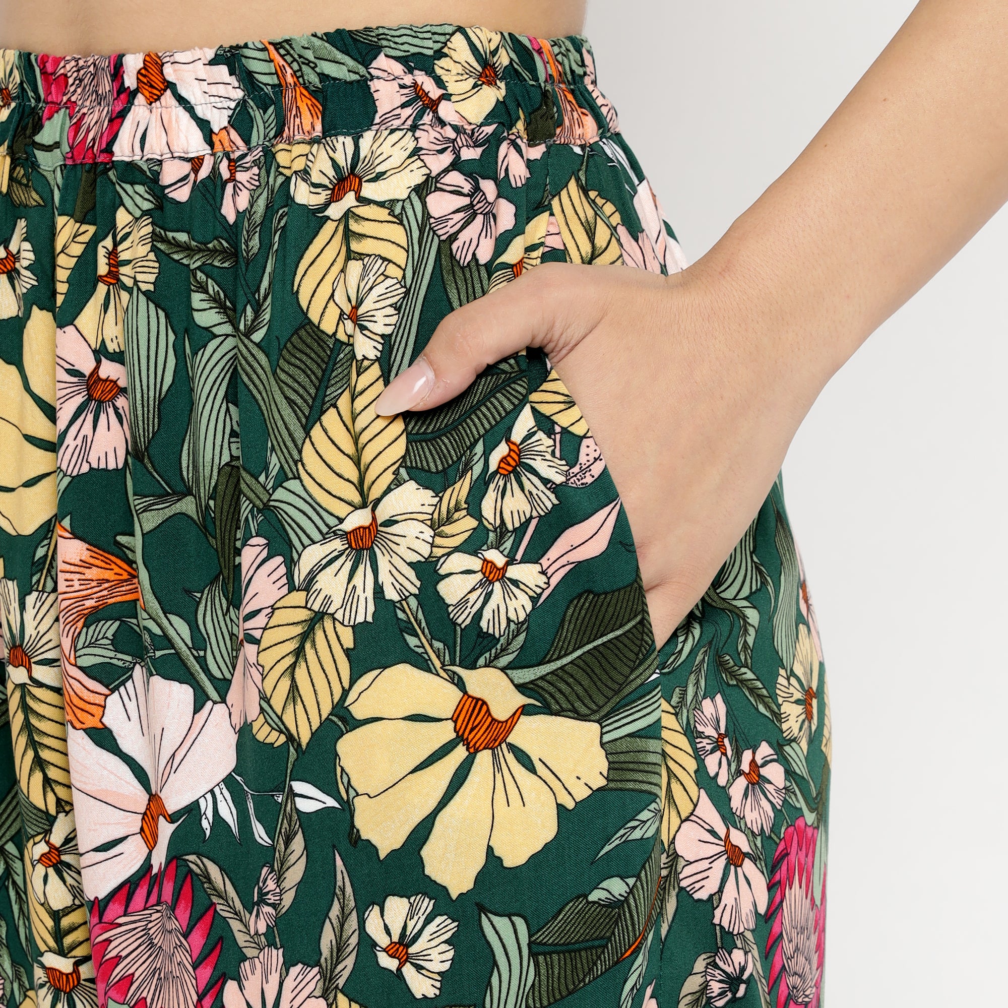 Close-up view of the Tropical Bloom Co-ord Set, featuring a high-waisted bottom with a dark green base and vibrant tropical floral prints in yellow, pink, red, and white. The design includes an elastic waistband and a side pocket, with a model’s hand placed inside the pocket to highlight the fit and comfort of the garment.
