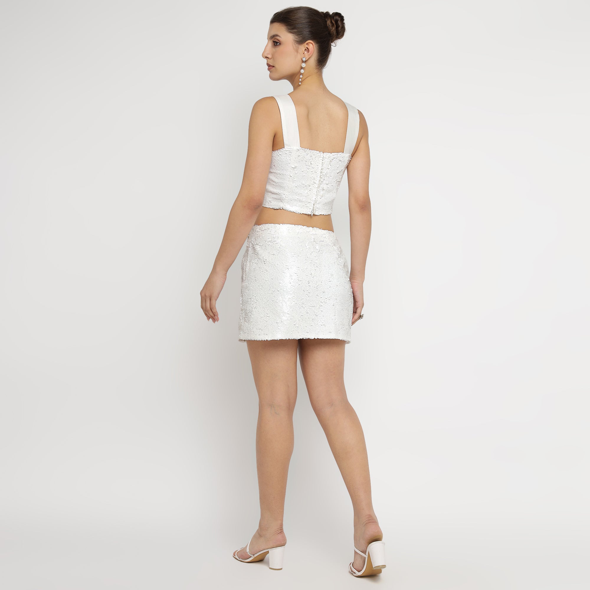 Back view of model in White Embellished Sequin Co-ord Set featuring sleeveless bow-strap crop top and matching mini skirt, paired with white heels.